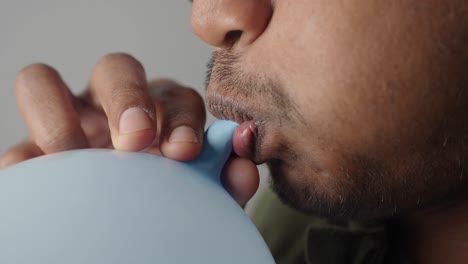 man blowing up a blue balloon