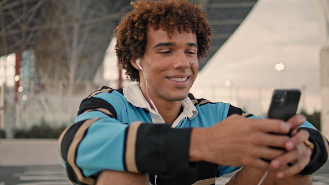 Curly student smiling smartphone at street closeup. Laughing blogger enjoying