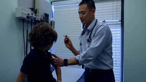 Vista-Lateral-De-Un-Joven-Médico-Asiático-Inyectando-Una-Jeringa-A-Un-Paciente-Niño-Caucásico-En-La-Clínica-4k