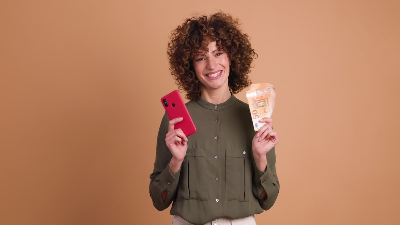 Donna entusiasta con contanti e cellulare in studio beige