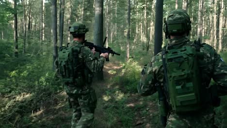 two soldiers in camouflage walk through a forest path, carrying weapons and tactical gear