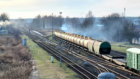 Tren-De-Carga-Que-Transporta-Camiones-Cisterna-En-Ferrocarril-Con-Telón-De-Fondo-Industrial,-Durante-El-Día