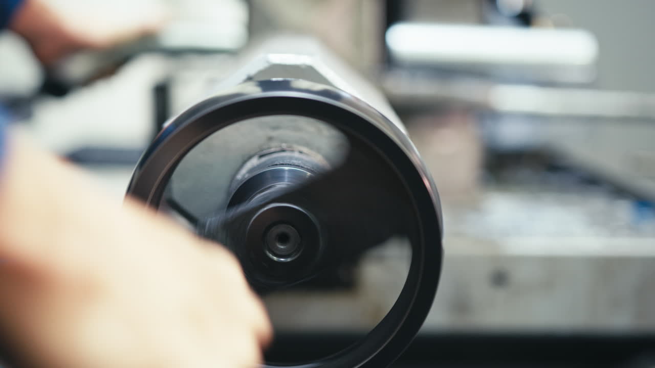 Worker rotating adjustment wheel on metal lathe tool wearing blue workwear. Slow motion.