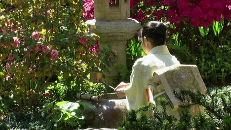 una mujer japonesa usa un cucharón de bambú frente a una linterna de piedra en un jardín japonés