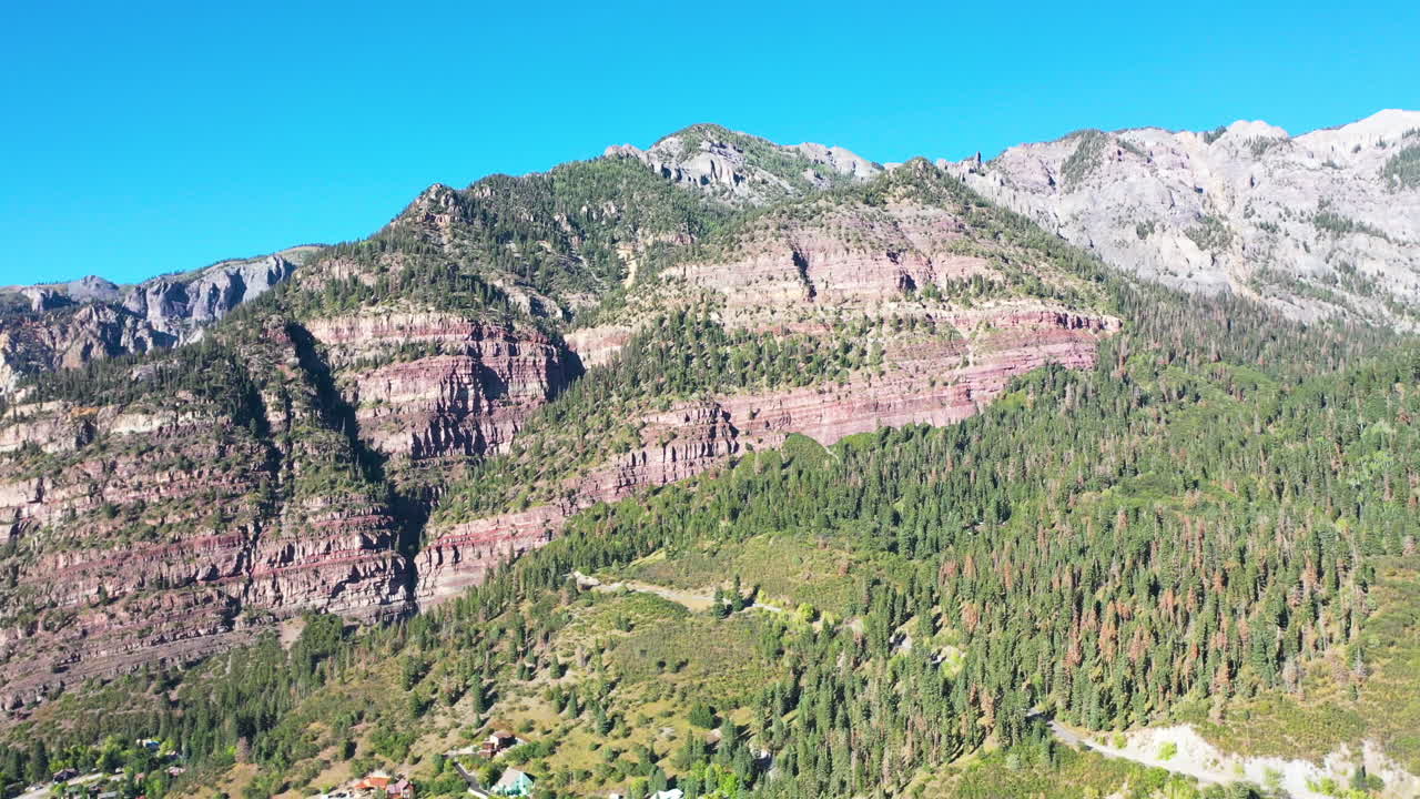 antena drone pan a la izquierda del hermoso bosque de pinos gruesos de ouray colorado y cordillera durante el verano con casas de pueblo de montaña rocosa y conducción de automóviles