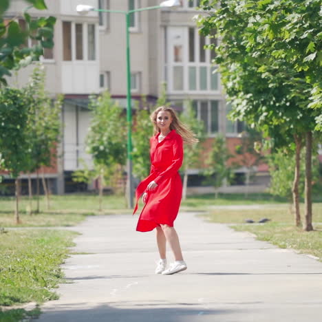 backside view of long-haired woman outdoors. pretty girl in red dress walking along the street and turns to camera with a smile. slow motion.