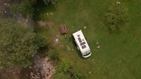 tourists with white van camp by the mountain river in green nature during a sunny day of summer - aerial top down