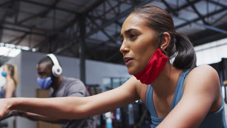 Frau-Mit-Gemischter-Rasse-Trägt-Eine-Abgesenkte-Gesichtsmaske-Und-Trainiert-Im-Fitnessstudio