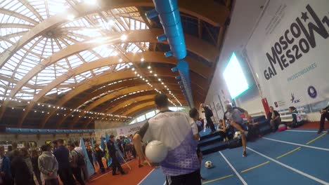 young male spinning soccer ball, dances around, indoor event, handheld