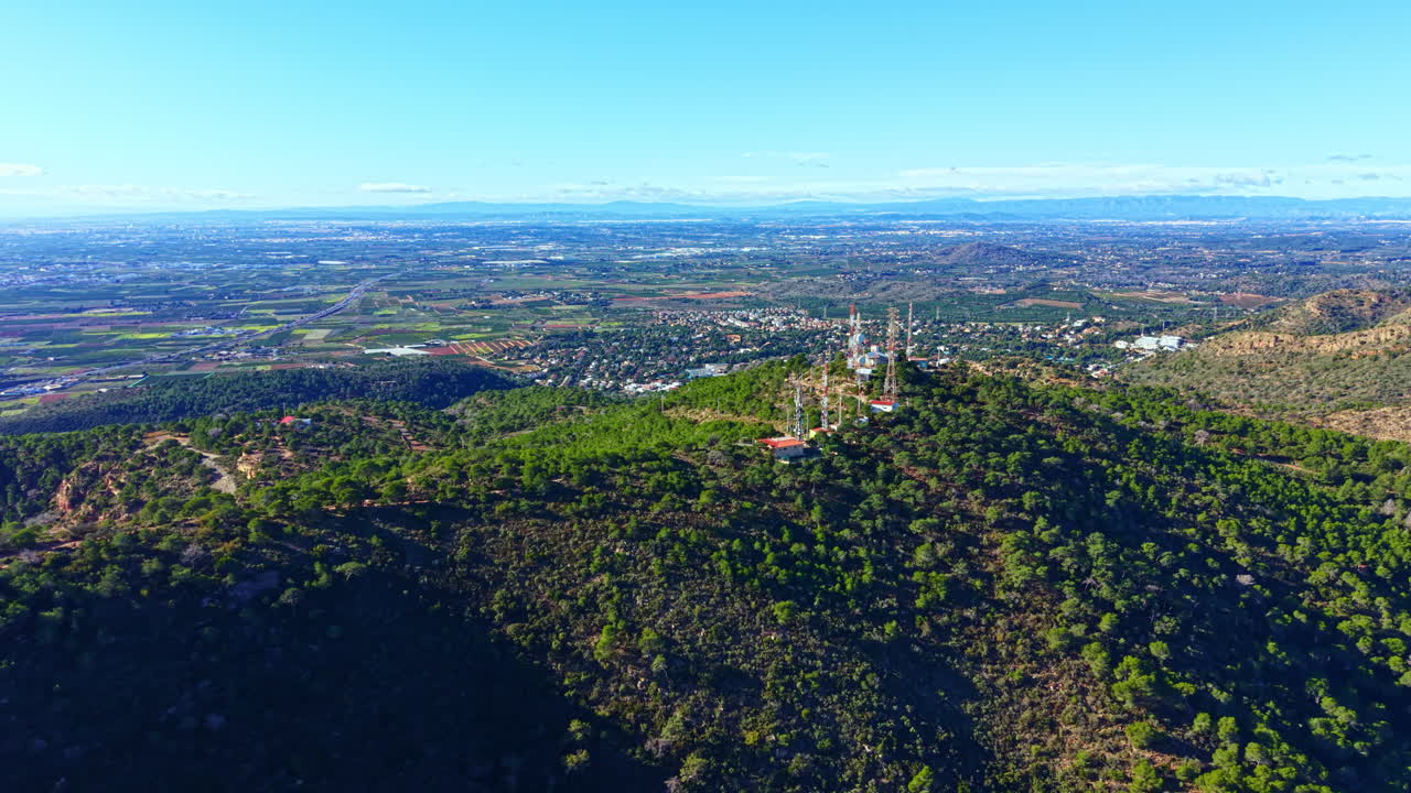 Veduta di una collina verde con torri di comunicazione e una città in lontananza in una giornata limpida