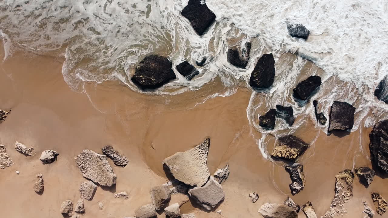 Ripresa aerea dall'alto di acqua che schizza su una spiaggia sabbiosa durante una giornata di sole