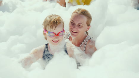 mom and her little daughter play with soap and foam in a crowd of tourists at a beach party in a res