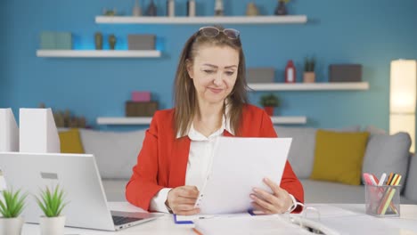 Home-office-worker-woman-smiling-at-camera-looking-at-paperwork.