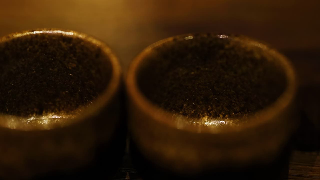 Close-up of liquid being poured into two brown, textured cups on a wooden surface.