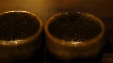 close-up of liquid being poured into two brown, textured cups on a wooden surface.