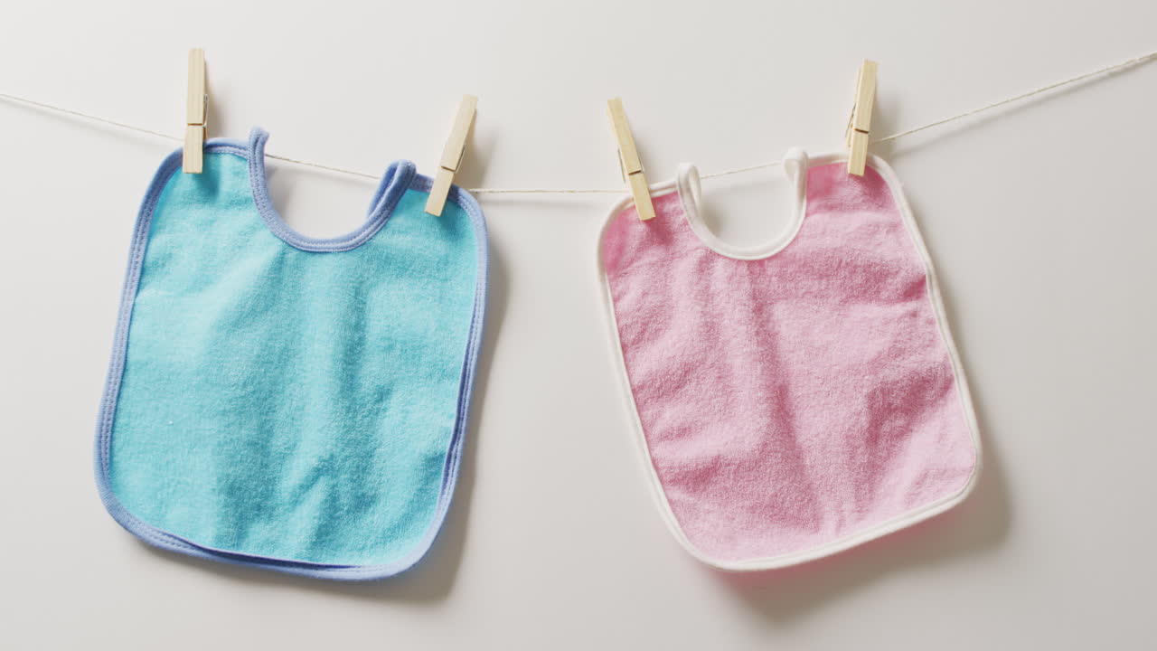 Video of close up of blue and pink bibs with pegs hanging on white background