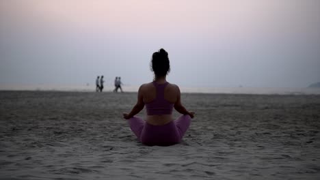 mujer india de yoga en posición de loto, medita en la playa al amanecer, al atardecer