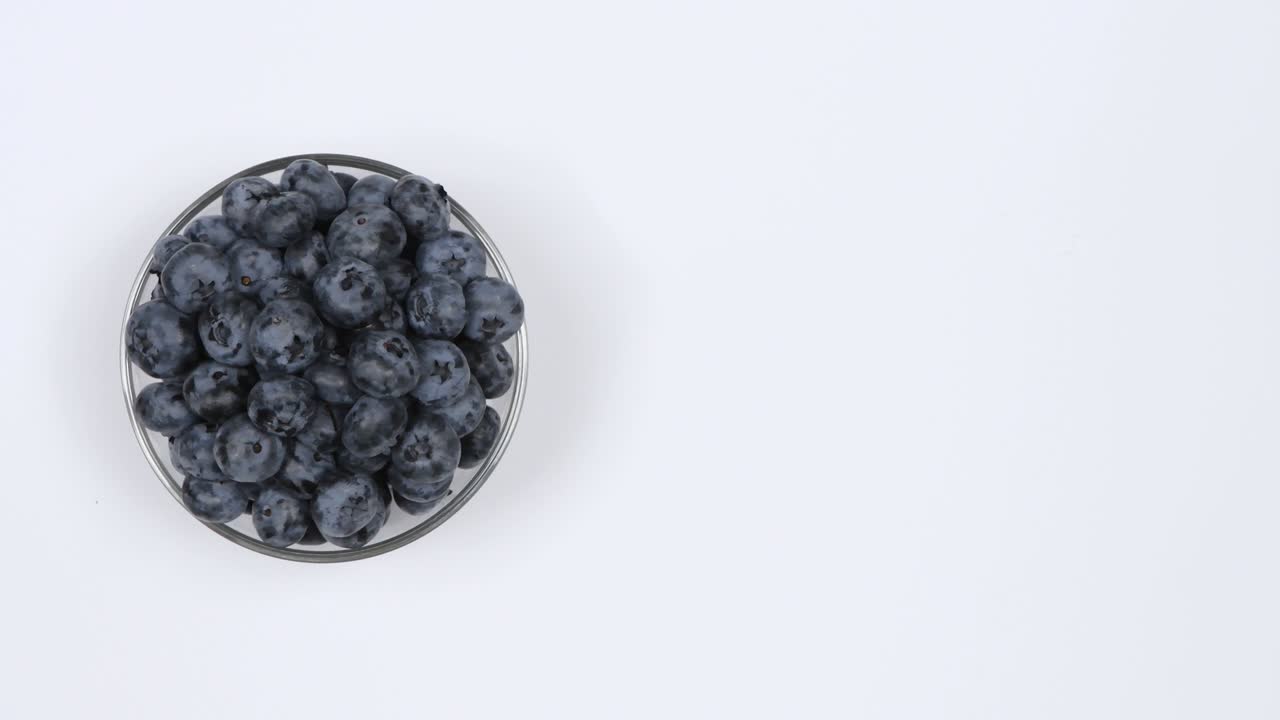 arándanos en un cuenco de vidrio sobre un fondo blanco. vista superior. movimiento de bucle. espacio libre a la derecha. rotación 360.