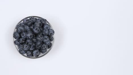 blueberries in a glass bowl on a white background. top view. loop motion. free space on the right. rotation 360.