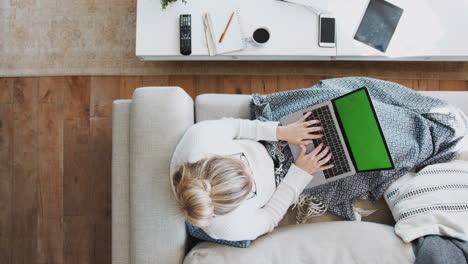 overhead shot looking down on woman working on laptop at home lying on sofa