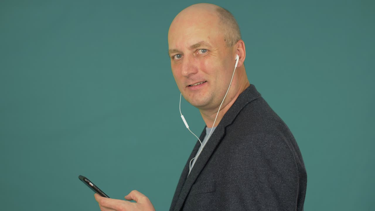 Uomo calvo che usa il cellulare per ascoltare musica con le cuffie, di profilo.