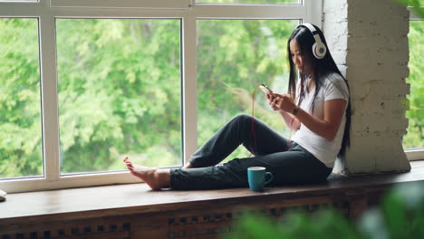 woman relaxing by the window with headphones and phone
