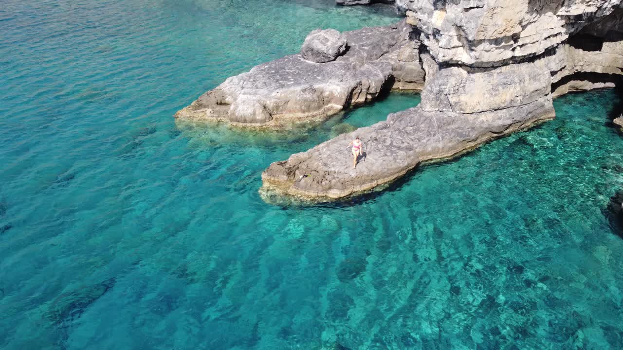 Orbit aerial drone view of a woman jumping in Turquoise crystal clear waters in Aspes beach, South Crete, Greece. Mediterranean Sea.