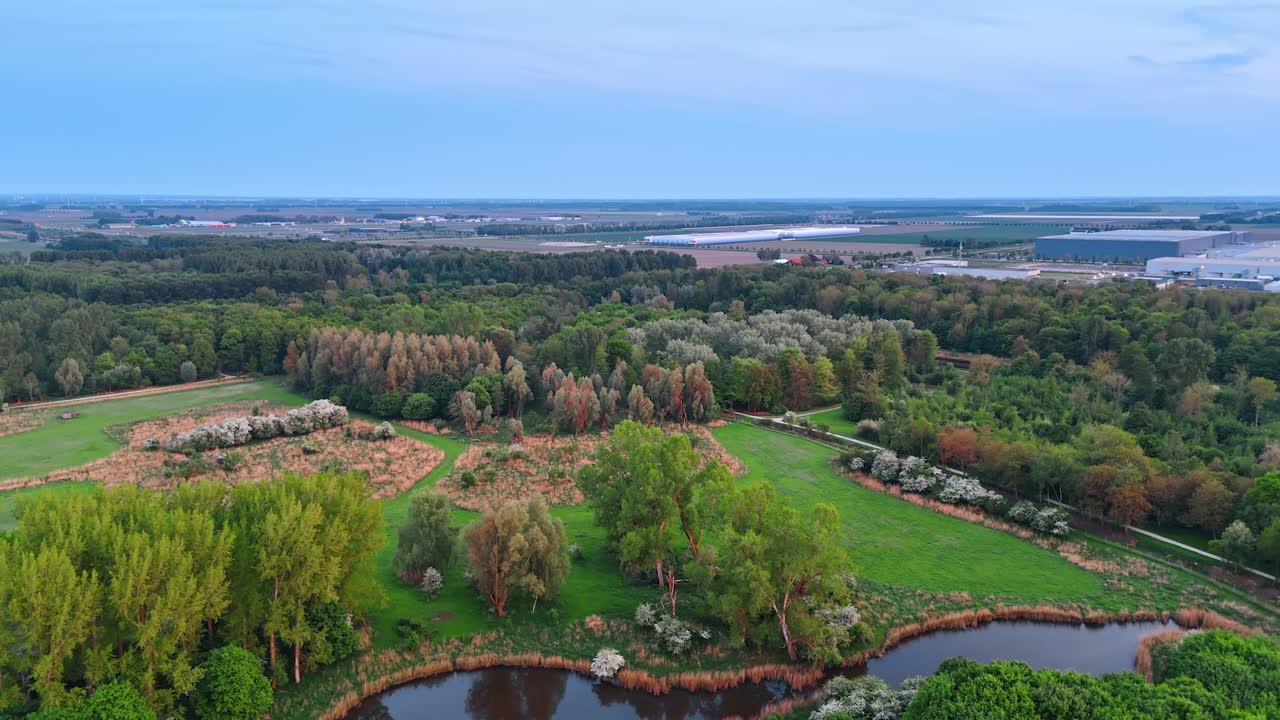 Vast agricultural fields, green forests and meadows in the countryside of the Netherlands. Storehouses at backdrop. Aerial view.