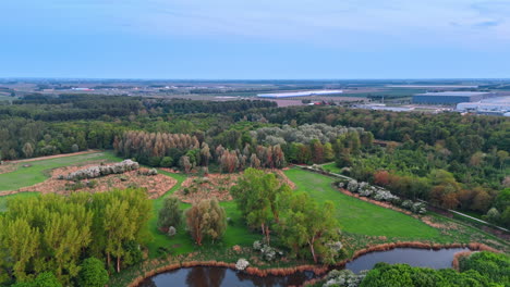vast agricultural fields, green forests and meadows in the countryside of the netherlands. storehouses at backdrop. aerial view.