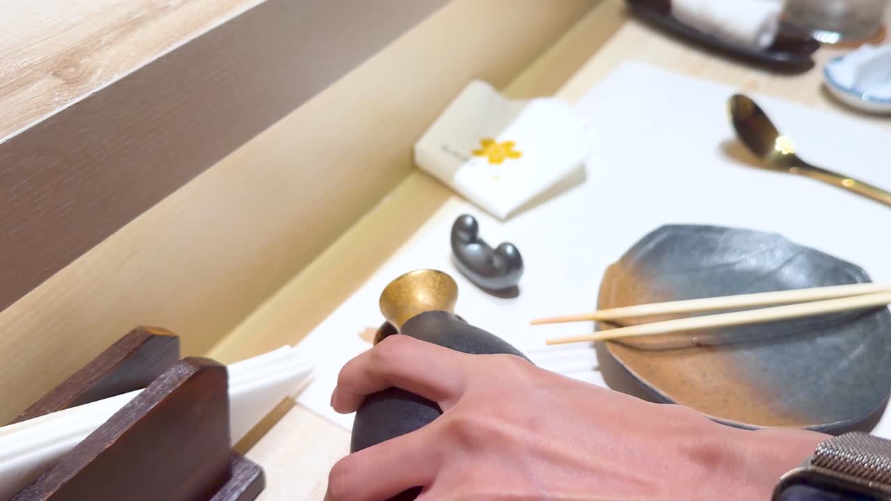 テーブルで手でカップにサケを注ぐ