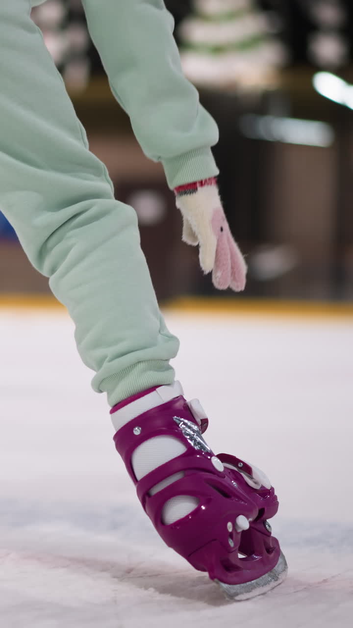 primer plano de una mujer patinando en una pista de hielo con patines púrpuras y traje verde menta, usando su mano en el hielo para el equilibrio, otros patinadores son visibles en el fondo