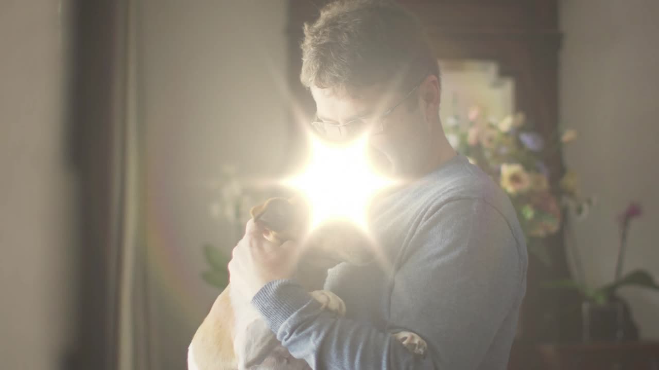 Uomo che culla un cane alla finestra, con un bagliore dell'obiettivo che attraversa e fa rannicchiare il cane, un sorriso caloroso per la cura dell'animale domestico.