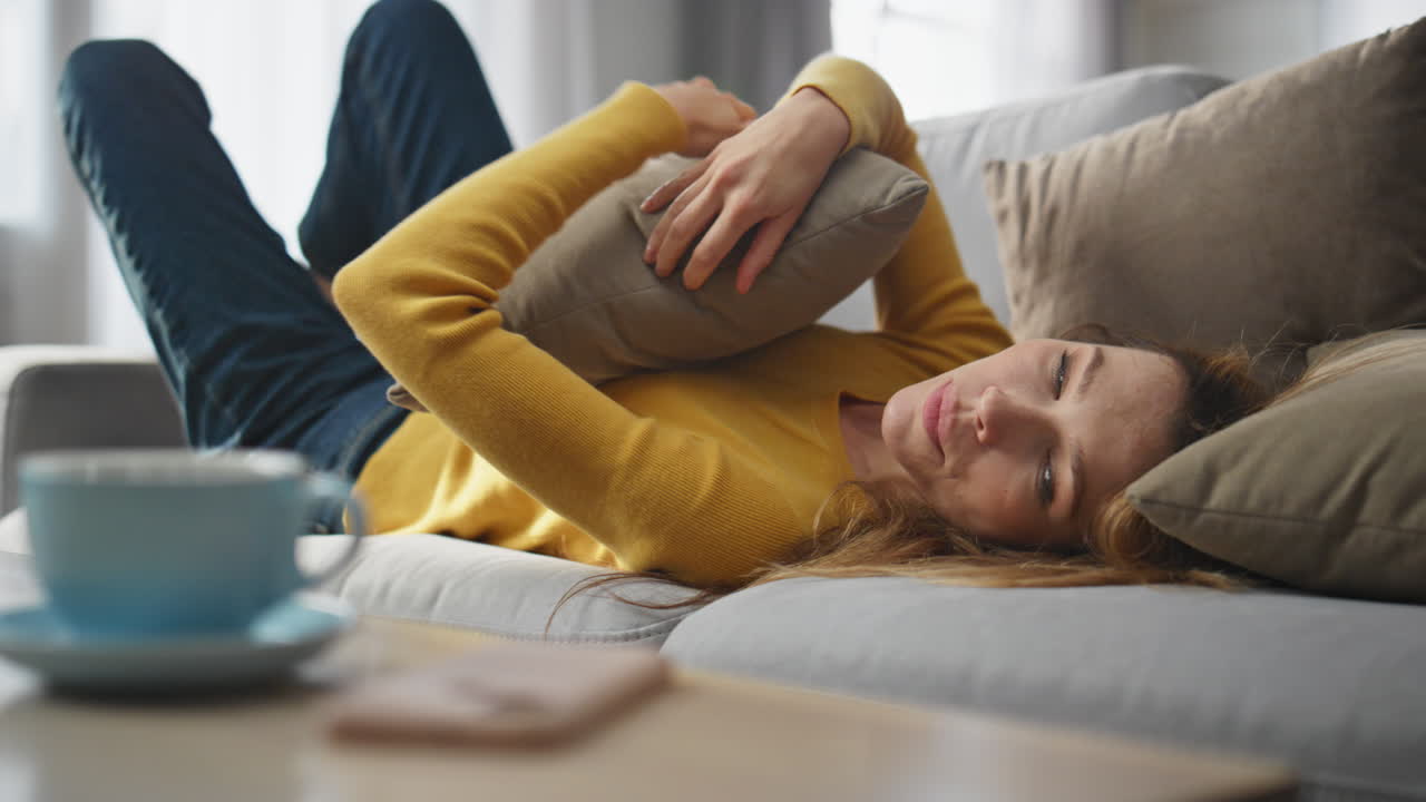 Joyful model falling couch hugging pillow at home closeup. Woman taking phone