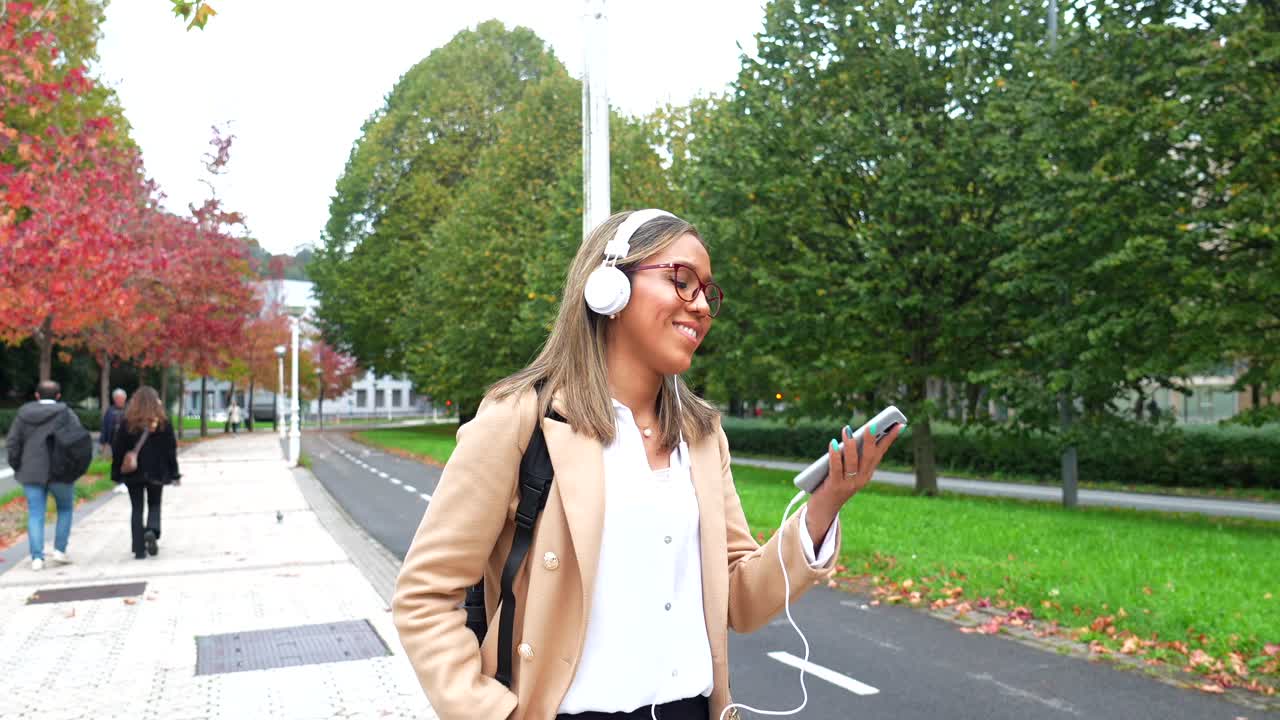Woman with headphones walking on a street in autumn park