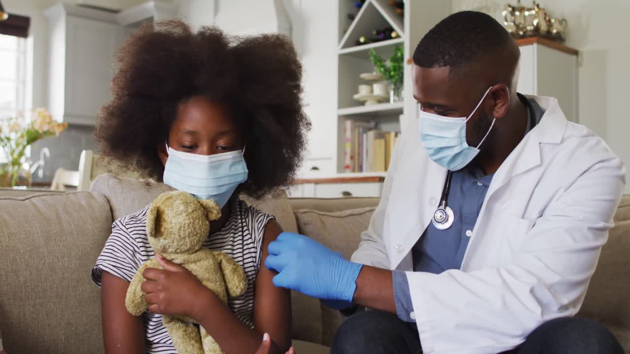 Medico afroamericano che indossa una mascherina e inietta il vaccino COVID-19 a una bambina a casa.