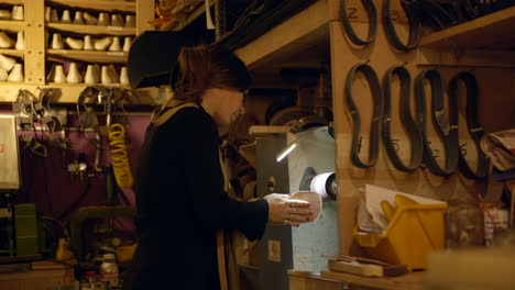 female shoemaker smoothing shoe sole working on old fashioned workshop grinding machine, medium shot