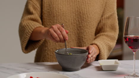 close up of woman at home in kitchen preparing healthy vegetarian or vegan meal pouring sauce onto bowl of tabbouleh salad with glass of wine