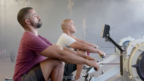 diverse group fitness class training hard on rowing machines at gym, in slow motion