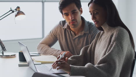 businesswoman working on laptop at desk with male colleague using digital tablet and stylus