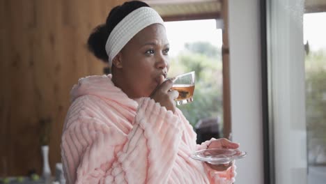 African-american-plus-size-woman-wearing-bathrobe-and-drinking-tea-at-spa,-unaltered,-slow-motion