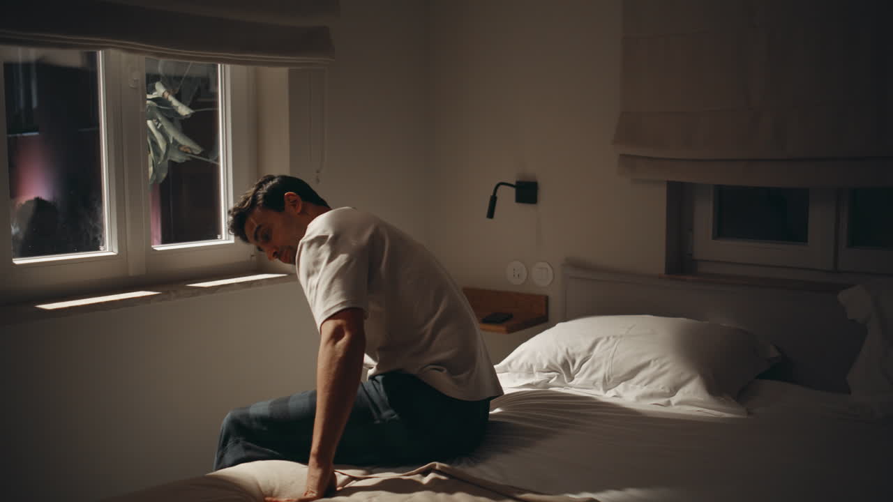 Sleepless guy holding mobile phone in dark bedroom. Tired man put down cellphone