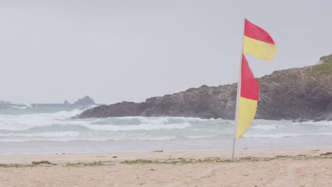 banderas amarillas y rojas de socorristas ondeando en el viento fuerte en la playa de cornwall