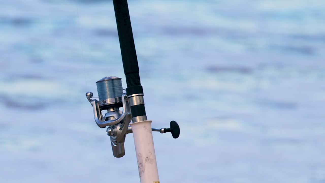 背景に波が打ち寄せるぼやけた海を伴う、釣竿のリールのクローズアップ。