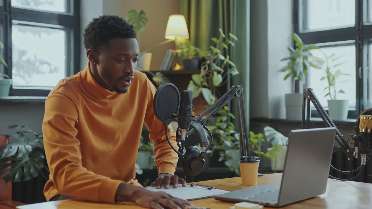 African American Podcaster Putting on Headphones and Talking in Mic in Studio