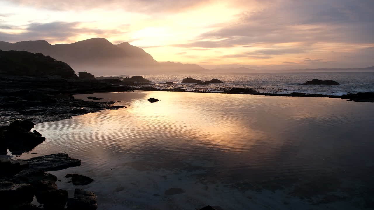 Vibrant sunrise sky in scenic Hermanus reflected in calm flat marine tide pool