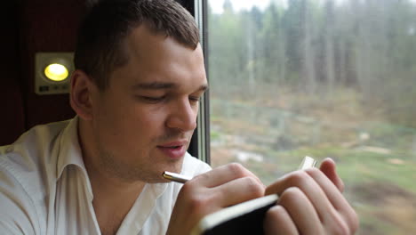 joven pensativo tomando notas en el tren