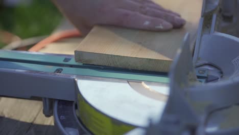 man's hands separating sawed off wooden piece from mitre saw