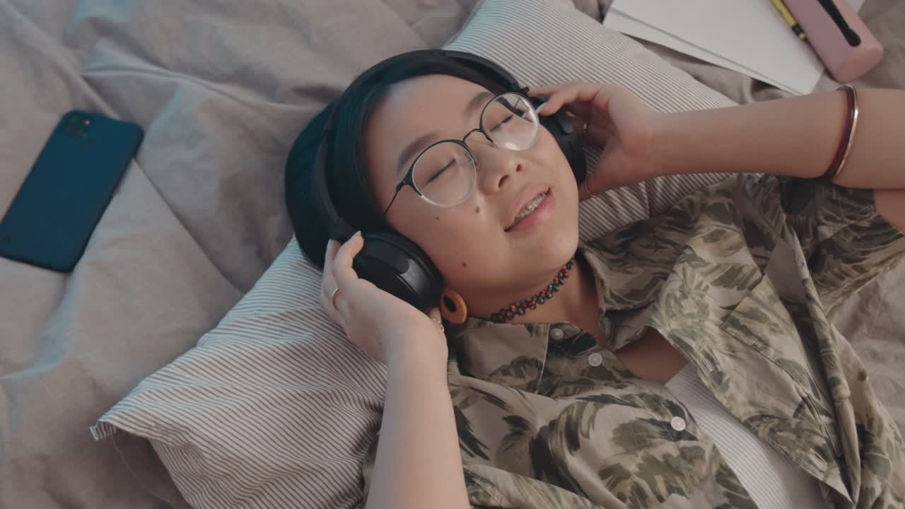 아시아 십대 소녀가 침대에서 헤드폰으로 음악을 듣고 있습니다.
