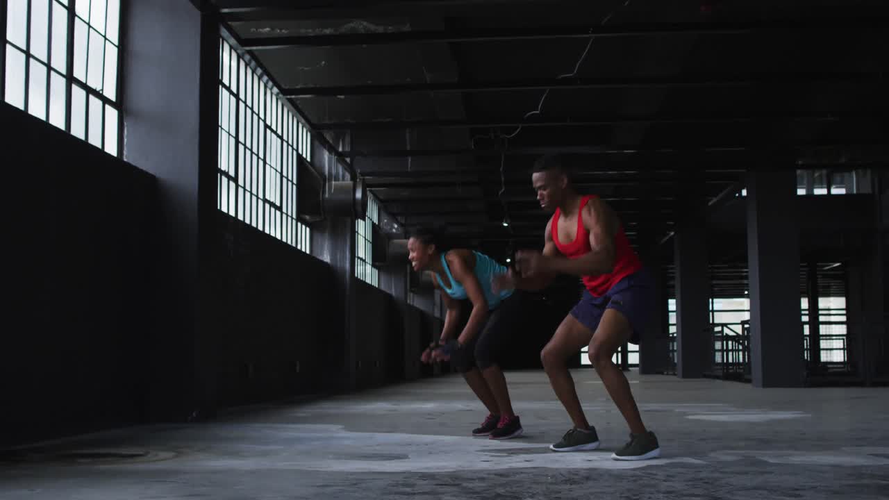 아프리카계 미국인 남성과 여성이 빈 도시 건물에서 푸시업 점프 운동을 하고 있습니다.