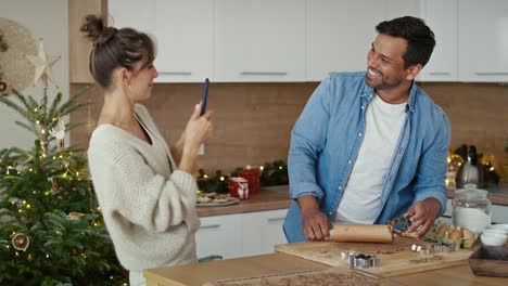 Nahaufnahme-Eines-Multiethnischen-Paares,-Das-In-Der-Weihnachtszeit-Lebkuchen-Backt-Und-Sein-Mobiltelefon-Benutzt.